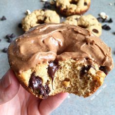 a hand holding a half eaten chocolate chip doughnut with one bite taken out of it