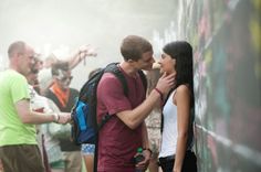 a man and woman standing next to each other near a wall with graffiti on it