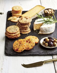 an assortment of cheeses, crackers and olives on a slate platter