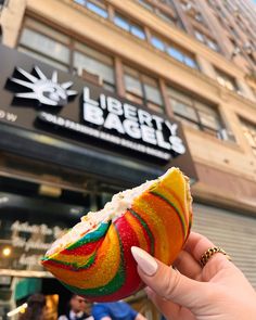 a person holding an apple in front of a building with a sign that reads liberty bagel