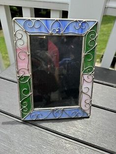 a small multicolored mirror sitting on top of a wooden table next to a white fence