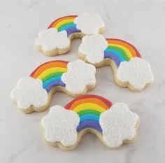 four rainbow cookies with white frosting on a marble countertop next to each other