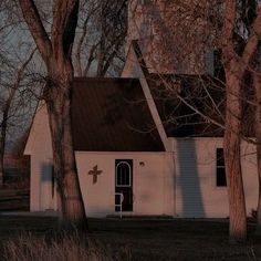 an old white church with a cross on the door and trees in front of it