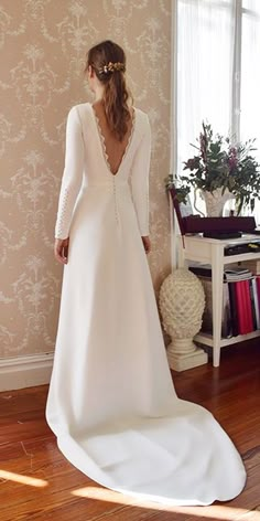 a woman in a white wedding dress standing on a wooden floor next to a window