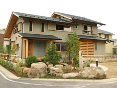 a house with rocks in front of it and trees on the side of the road