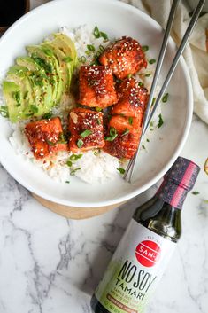 a white bowl filled with meat and rice next to a bottle of booju sauce