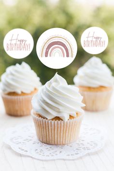 three cupcakes with white frosting and rainbow toppers on a doily