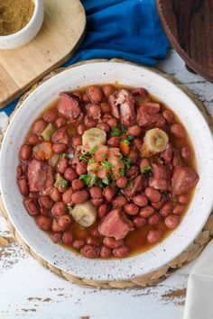 a white bowl filled with beans and meat next to a wooden spoon on top of a table