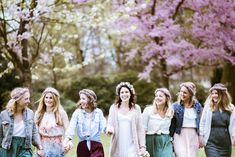 a group of women standing next to each other in front of trees with pink flowers