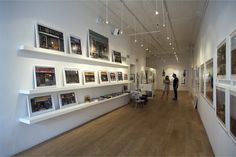 two people standing in an art gallery looking at pictures on the wall and shelves above them