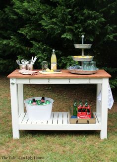 an outdoor picnic table with drinks and snacks on it, in front of some trees