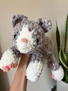 a crocheted cat is being held up by someone's hand next to a potted plant