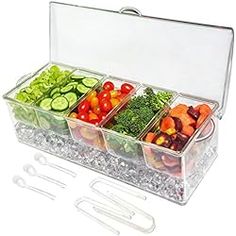 a plastic container filled with lots of different types of vegetables next to utensils