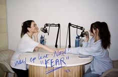 two women sitting at a table with microphones in the background and writing on the table