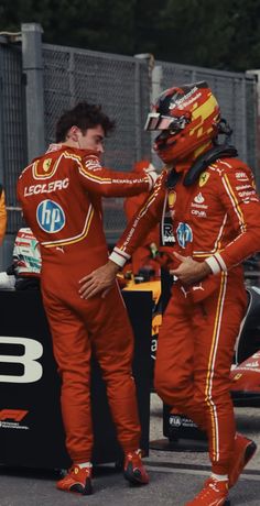 two men in red racing suits standing next to each other