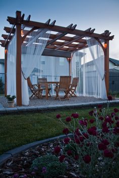 an outdoor dining area is lit up at night with flowers in the foreground and a pergolated roof