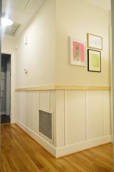 an empty room with wood floors and white walls, framed pictures on the wall above it