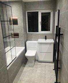 a white toilet sitting in a bathroom next to a bath tub and sink under a window