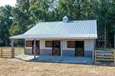 a horse barn in the middle of a field with two stalls and a fence around it