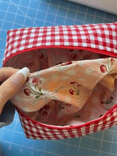 someone is sewing on the inside of a red and white checkered fabric bag with scissors