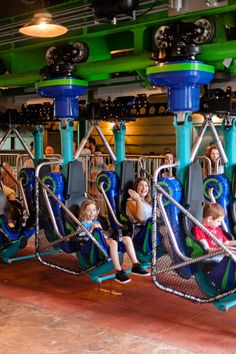 several children are sitting on swings in an indoor area with green and blue lights hanging from the ceiling