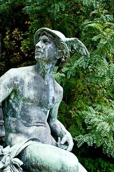 a statue of a man sitting on top of a bench in front of some trees