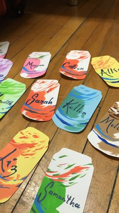 several different colored paper plates with names on them sitting on a wooden table next to each other