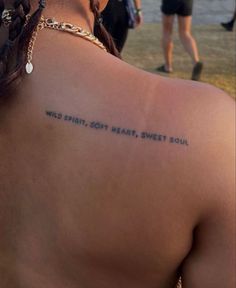 the back of a woman's neck with words written on it and people walking in the background