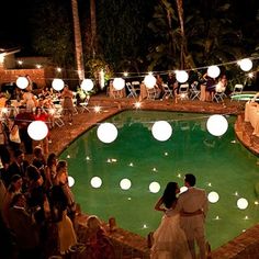 a couple standing next to each other in front of a pool surrounded by paper lanterns