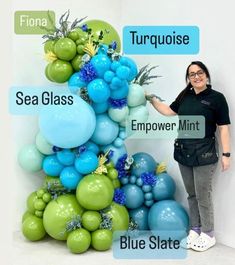 a woman standing in front of a tall display of blue and green balloons with the words sea glass emporer mint