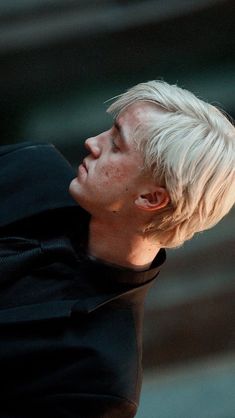 a young man with white hair and black shirt looking up at something in the air