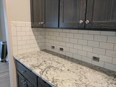 a kitchen with marble counter tops and dark wood cabinetry, along with white subway backsplash tiles