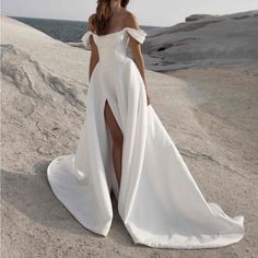 a woman standing on top of a sandy beach wearing a white dress with thigh high slit