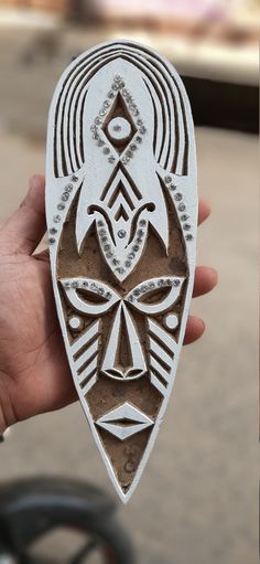 a person holding up a carved wooden object with designs on it's face and eyes