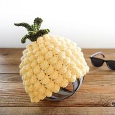 a crocheted pineapple sitting on top of a wooden table next to sunglasses