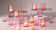 many different colored candles sitting in front of each other on a white surface with one candle lit