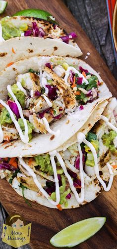 three tacos on a cutting board with lime wedges