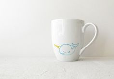 a white coffee cup with a blue and yellow whale design on the side, sitting on a table