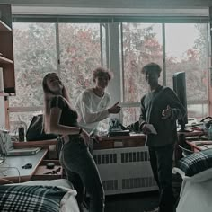 two people standing in a room with lots of clutter on the floor and windows