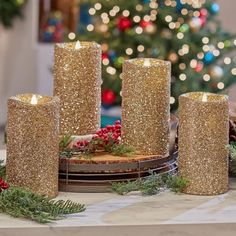 three gold glitter candles sitting on top of a table next to christmas decorations and a tree