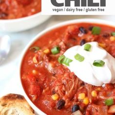 two bowls of chili with sour cream on top and bread in the foreground next to them