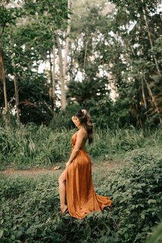 a woman in an orange dress is sitting on the grass and looking up into the sky