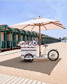 an ice cream cart is parked on the beach with umbrellas over it's doors