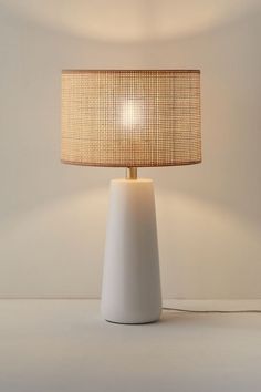 a white table lamp with a beige shade on it's base and a light bulb in the middle