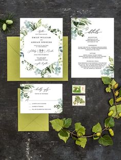 the wedding stationery is set up with greenery and green foliage, including leaves