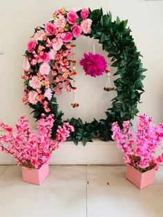 pink flowers are arranged in flower pots on the floor next to a wall with a wreath