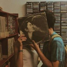 a man holding up a record in front of a woman's face with an album on it