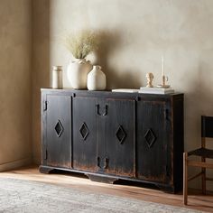 a black cabinet sitting on top of a wooden floor next to a chair and vase