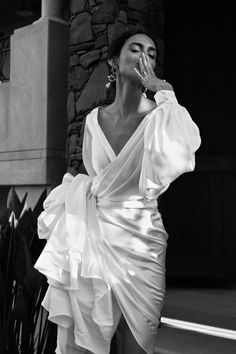 black and white photograph of woman in dress leaning against wall with hand on face, looking to the side