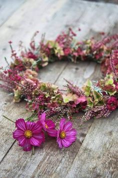 purple flowers and greenery are arranged in a wreath on an old wooden surface with planks